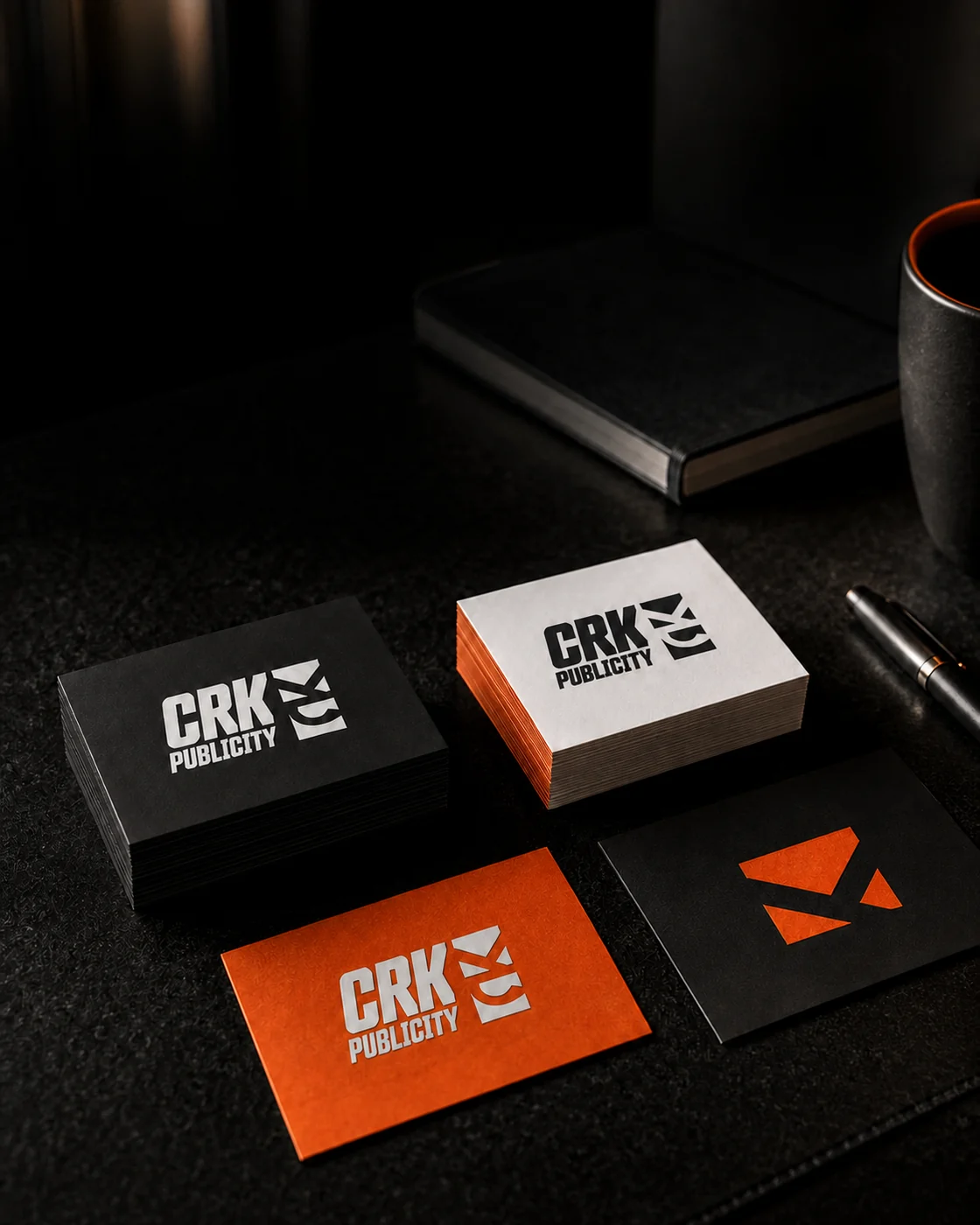Tarjetas de negocio CRK Publicity en acabados negro, blanco y naranja sobre una mesa de trabajo